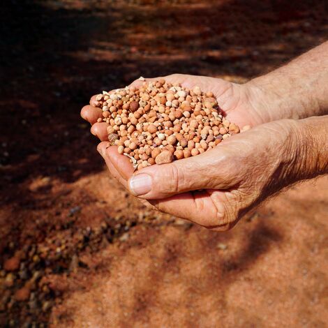 Deux mains tenant du minerai de bauxite dans un champ sablonneux.