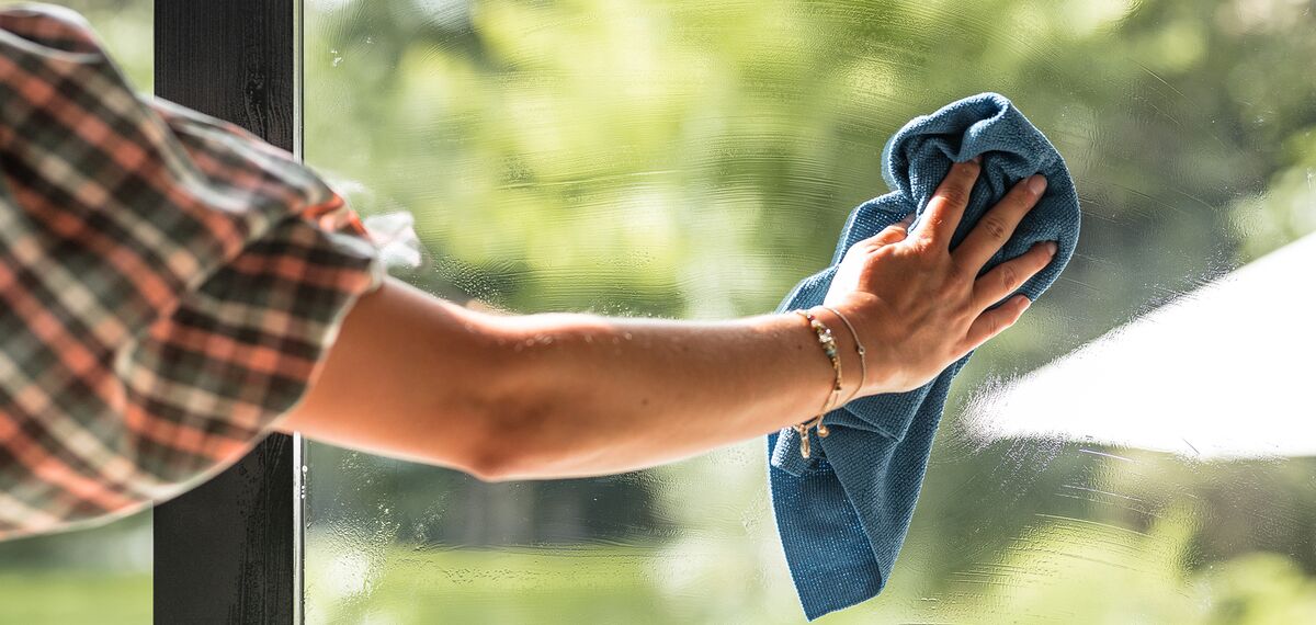 Vrouw poetst glas van Reynaers Aluminium raam met microvezeldoek
