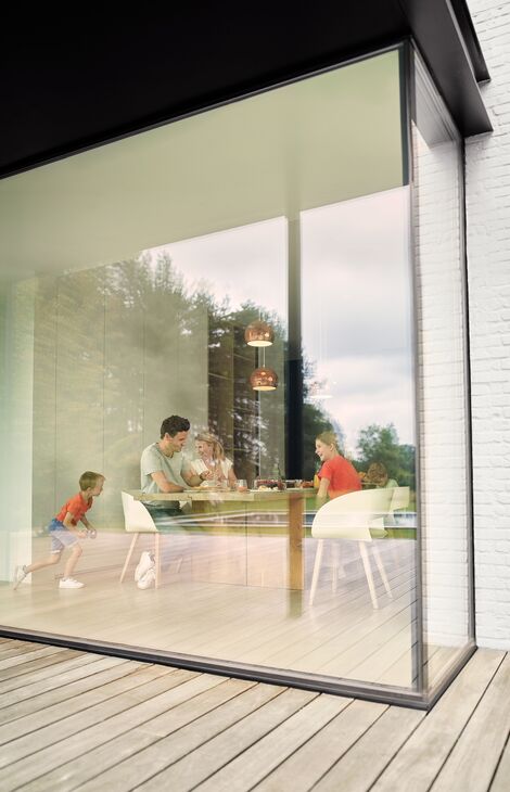 Gezin zit aan tafel en kijkt naar buiten door aluminium raam