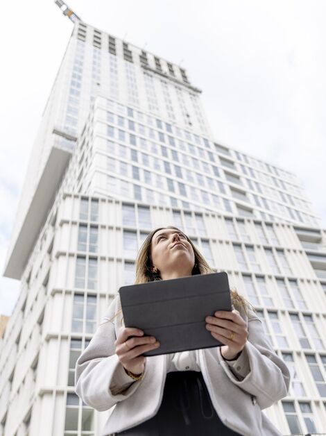 Femme blonde tenant un iPad regardant vers l’immeuble d’appartements blanc.