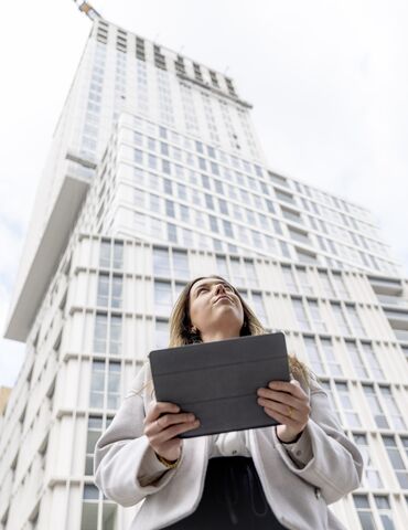 Femme blonde tenant un iPad regardant vers l’immeuble d’appartements blanc.