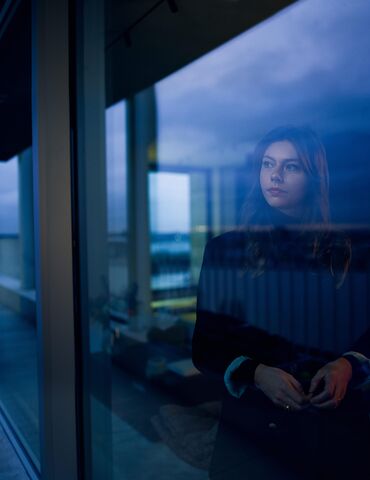 Femme regardant par la fenêtre à la tombée de la nuit.