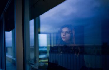 Femme regardant par la fenêtre à la tombée de la nuit.